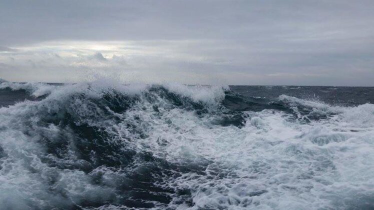 Close up of Scotland's wild sea, showing dark blue ocean waves with white sea foam on surface. Cloudy sky features in the background horizon.