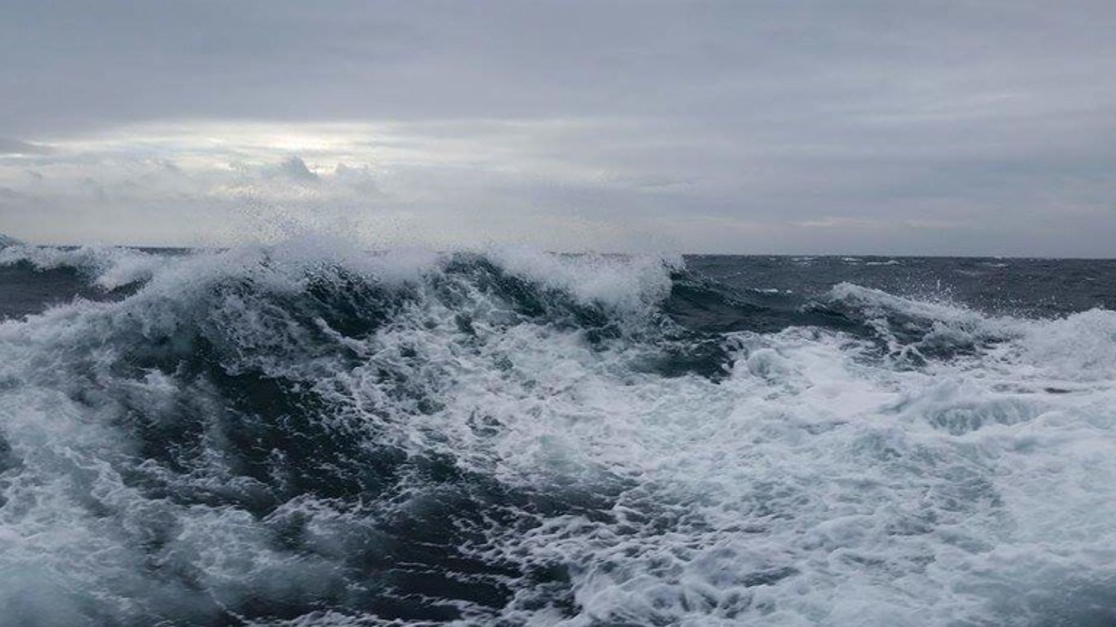 Close up of Scotland's wild sea, showing dark blue ocean waves with white sea foam on surface. Cloudy sky features in the background horizon.