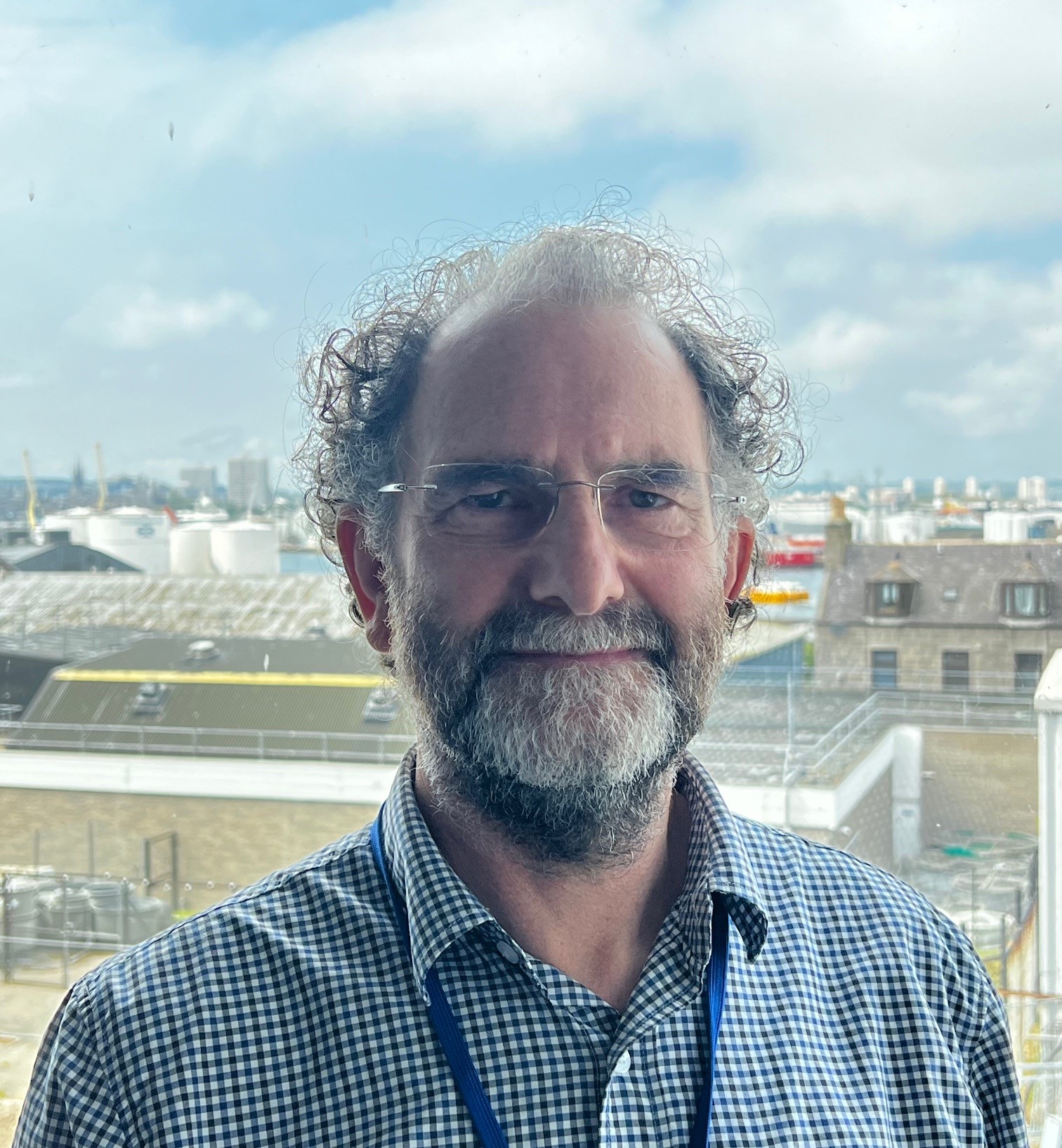 The image shows Mark Inall in a blue shirt against a harbour background.