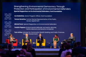 Three men and two women are seated on a raised stage in discussion.