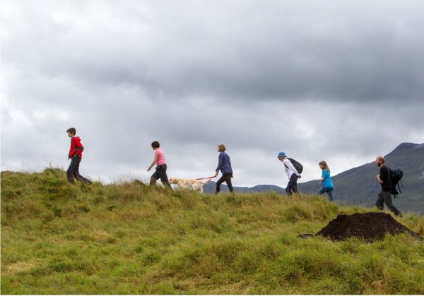 6 people and a dog walking up a hill, one following the other