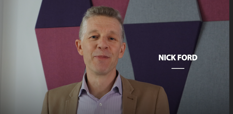 Still shot from the vlog of Nick Ford smilin in front of a purple background