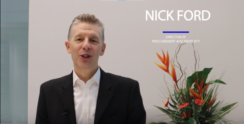 Nick Ford standing in front of a white wall, with colourful plant in the background